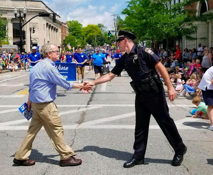 Governor Mike DeWine shaking hands with police officer on the parade route.